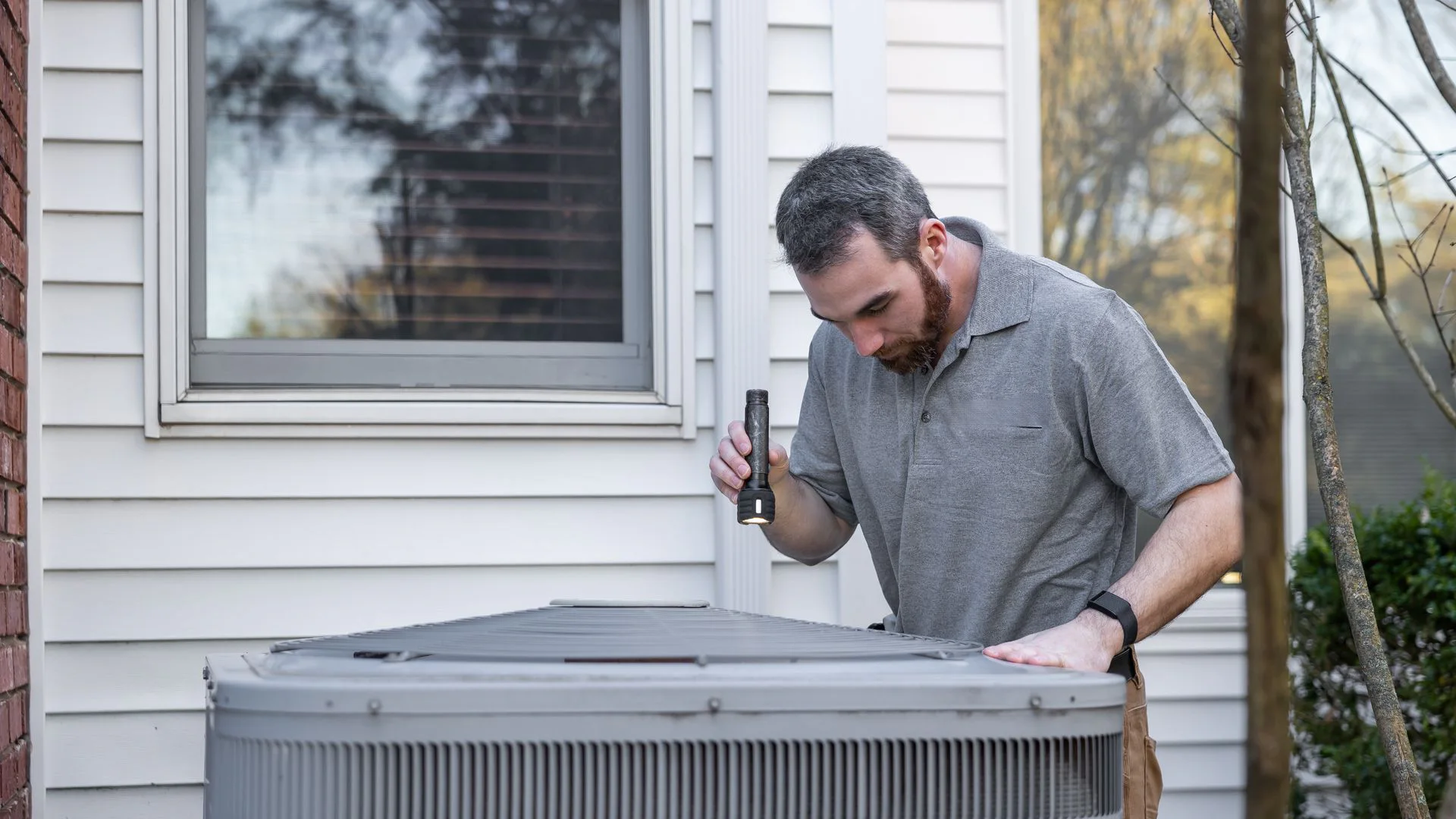 A technician inspecting an outdoor residential air-conditioning unit.