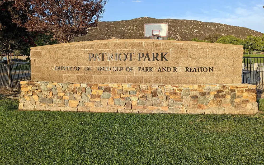 The stone sign for Patriot Park in 4S Ranch, with a lawn and a hill behind it