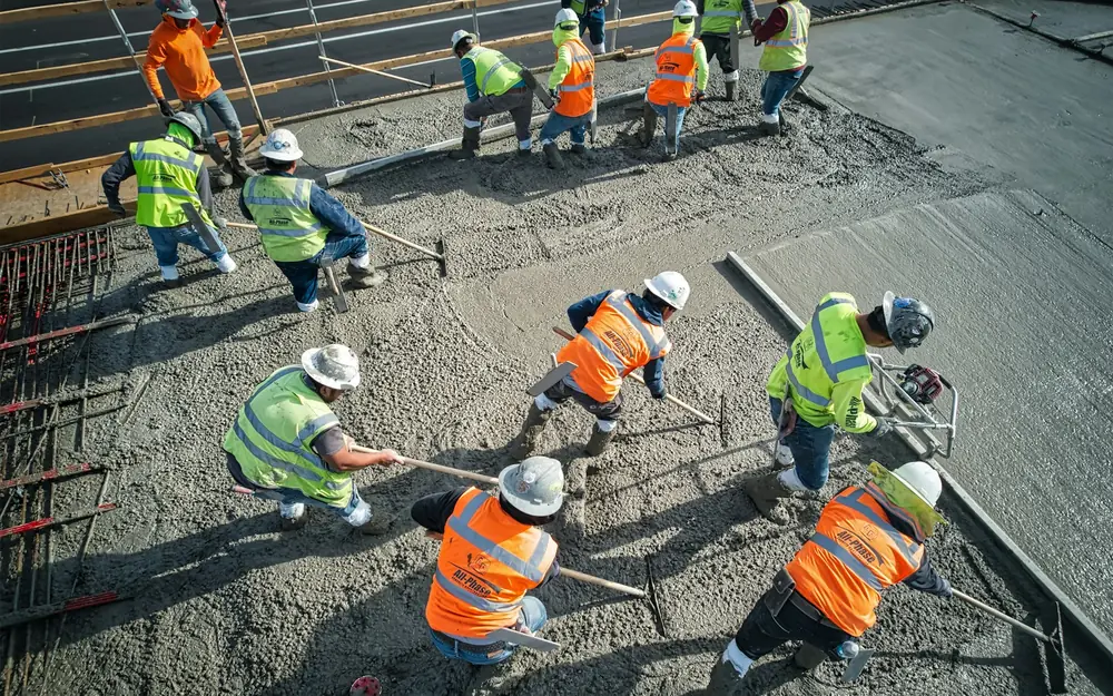 A crew in hard hats spreading and leveling freshly poured concrete, seen from above