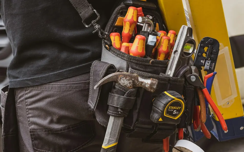 A worker with a full tool belt carrying a ladder