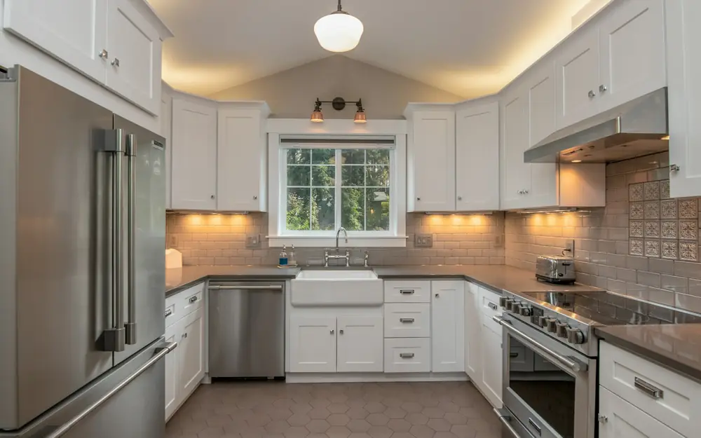 A remodeled kitchen with white cabinets, a farmhouse sink and under-cabinet lights