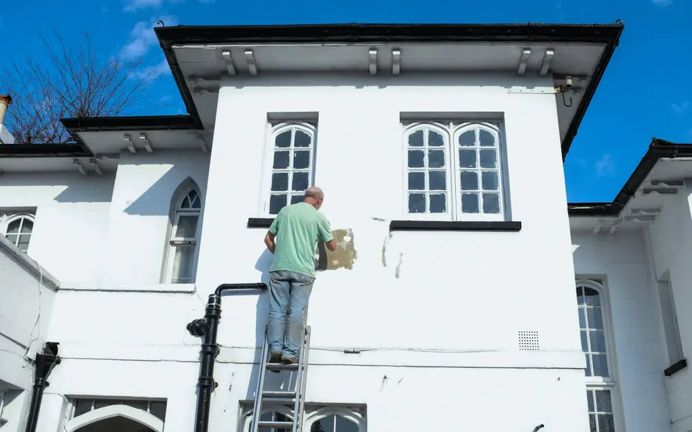 A painter on a ladder painting the outside of a white house