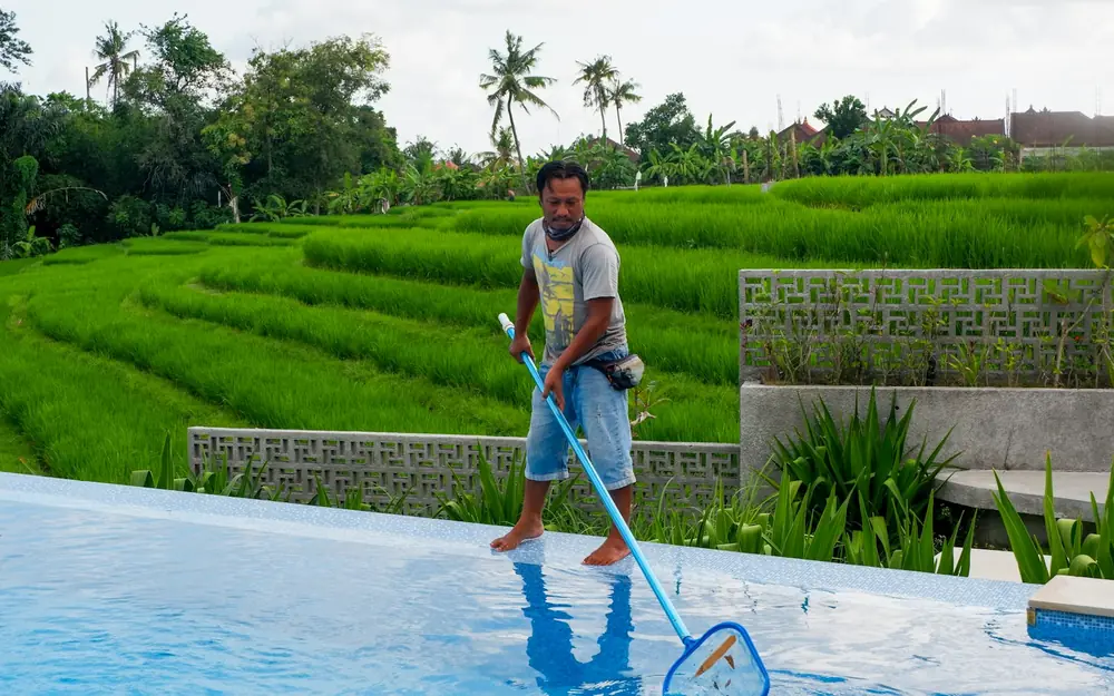 A worker skimming a swimming pool with a net