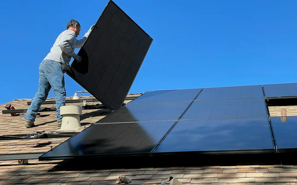An installer lifting a solar panel into place on a shingle roof