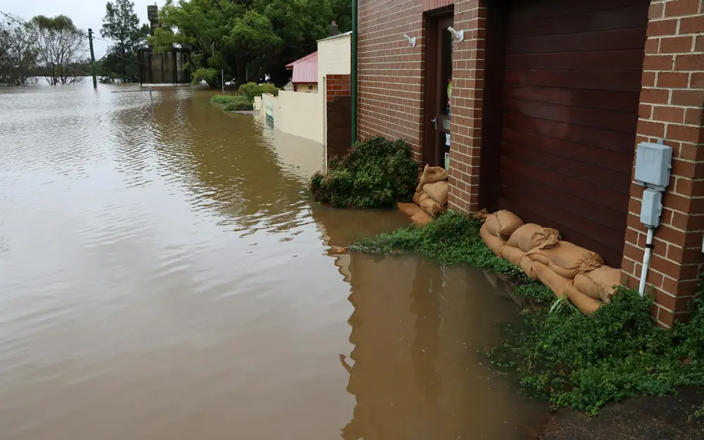 Floodwater up against a brick house, with sandbags at the door